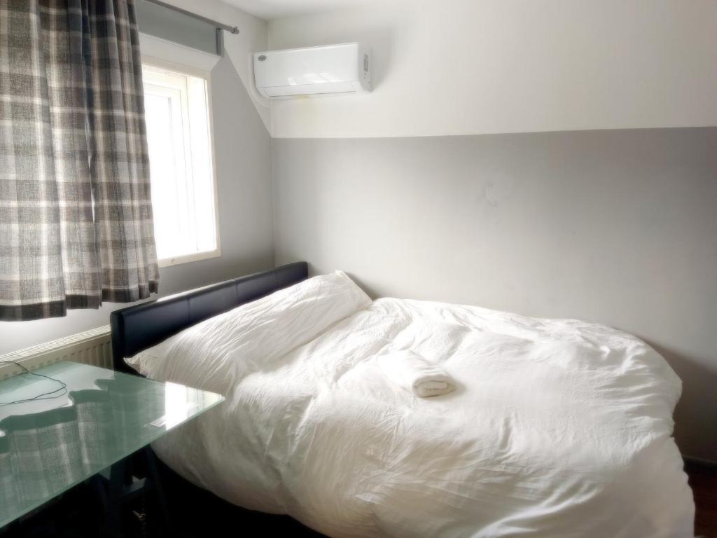 a white bed in a room with a glass table at Luxurious En-suite Soft Water Air Conditioning TV ETHERIUM in London