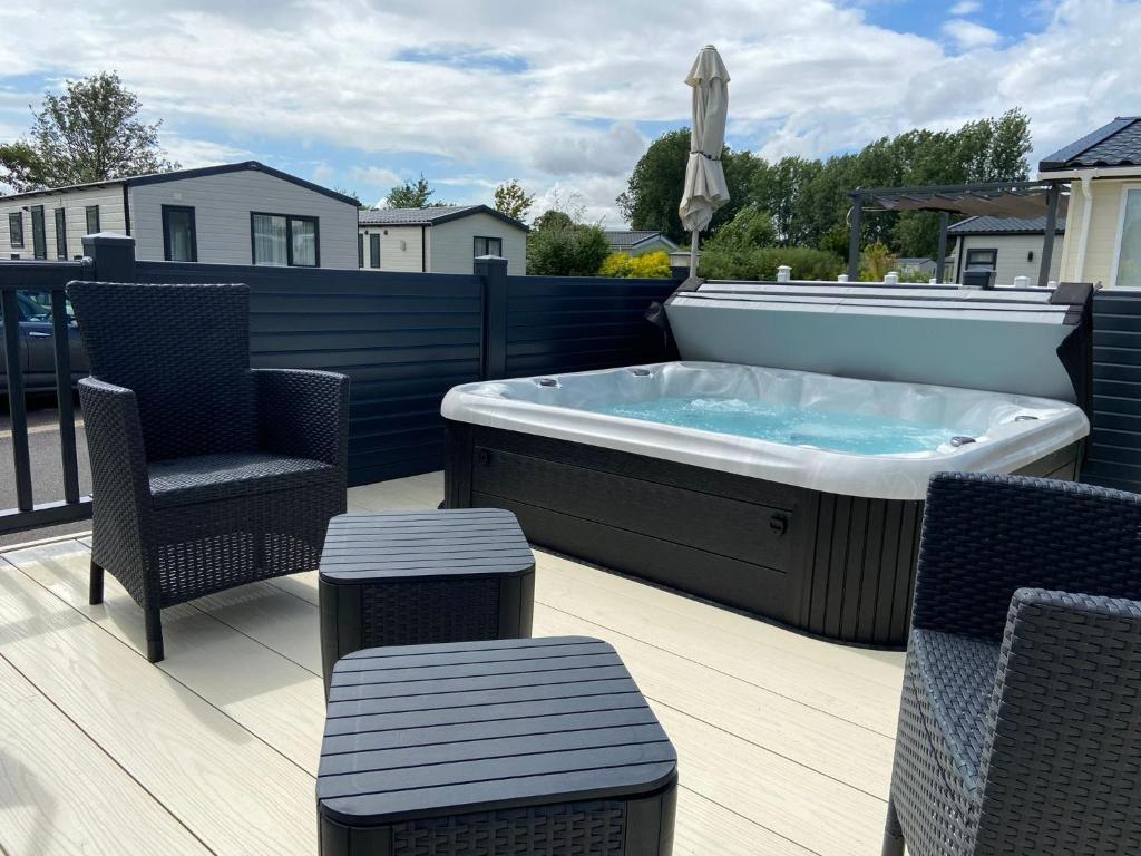 a hot tub on a deck with two chairs and a table at Hot Tub Lodge in the Cotswolds - Pet Friendly in South Cerney