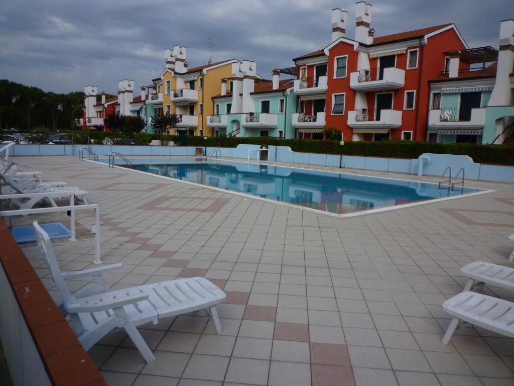 a swimming pool with white chairs and some buildings at Le Briccole in Cavallino-Treporti