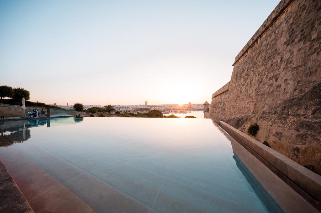 une piscine d'eau à côté d'un mur en pierre dans l'établissement The Phoenicia Malta, à La Valette