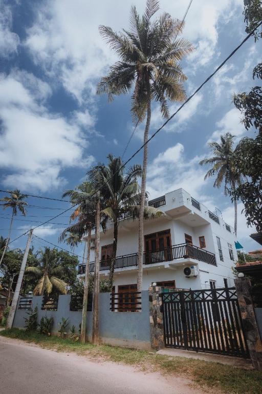 a white house with palm trees in front of it at RIU Villa & Apartment in Matara