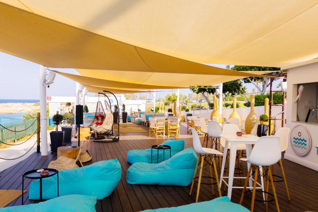 a patio with blue chairs and tables and a yellow umbrella at Cavo Maris Beach Hotel in Protaras