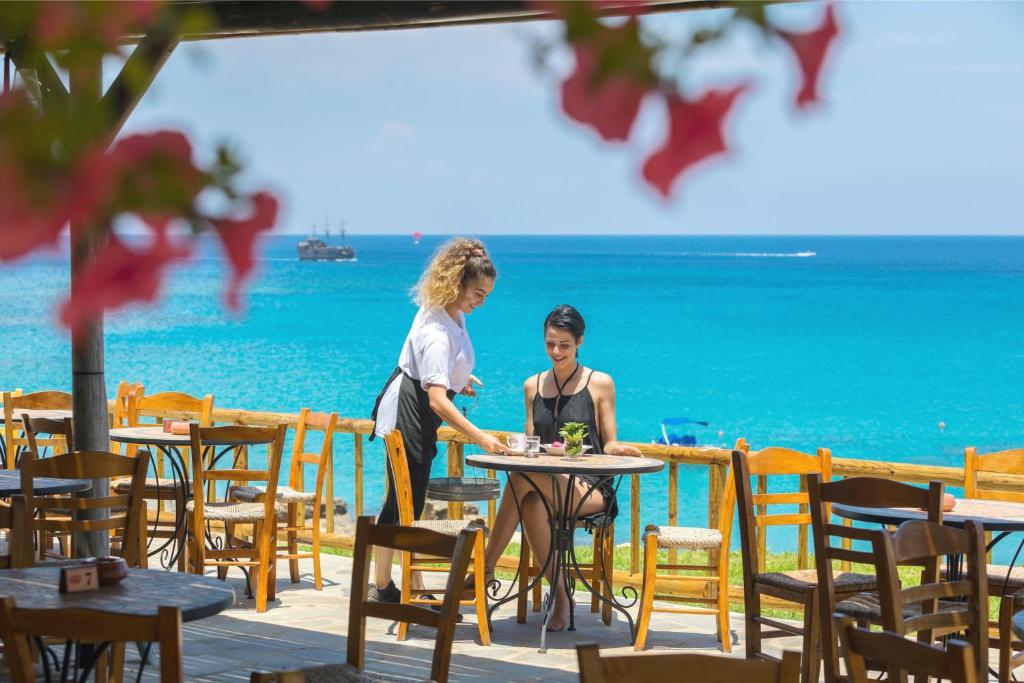 a man and a woman standing at a table near the ocean at Cavo Maris Beach Hotel in Protaras