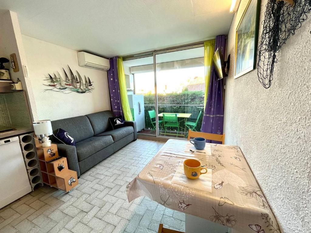 uma sala de estar com um sofá e uma mesa em Studio cabine avec piscine au Grau du Roi em Le Grau-du-Roi