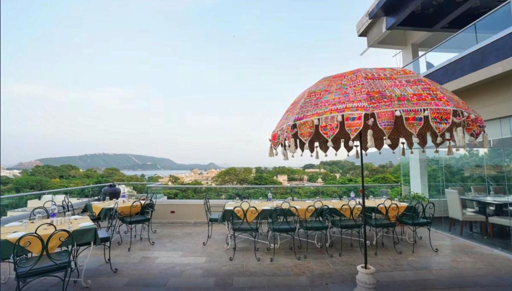 um pátio com mesas e cadeiras e um guarda-sol em The Ramvilas - A Rooftop Pichola Lake View Hotel em Udaipur