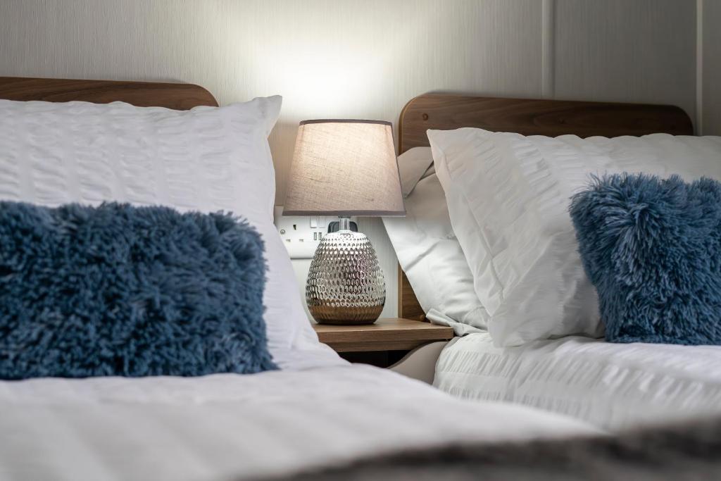 Port Seton的住宿－Seton Sands-3 Bed Static Caravan，一张带蓝色枕头的床和一张桌子上的台灯