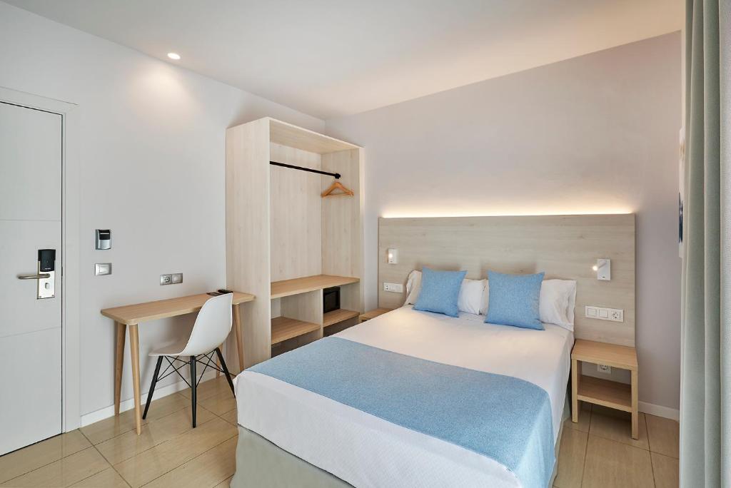 a bedroom with a bed with blue pillows and a desk at URH Excelsior in Lloret de Mar