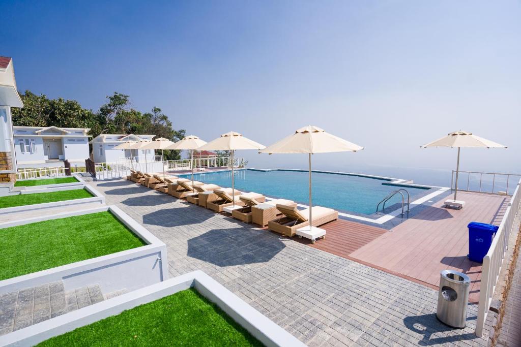 uma piscina com guarda-sóis e cadeiras e o oceano em Mawseintyllang Resort em Shillong