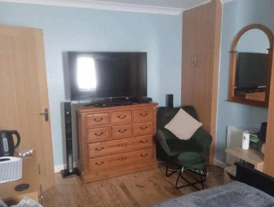 a bedroom with a dresser with a television and a chair at Daves guest room with use of local gym in Featherstone