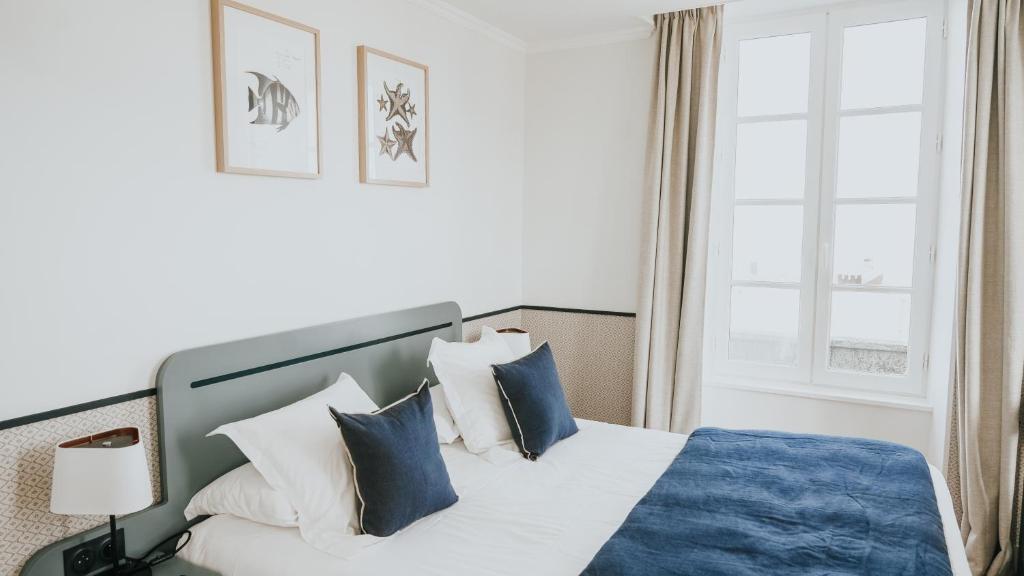 a bedroom with a bed with blue and white pillows at Hôtel De La Marine in Arromanches-les-Bains