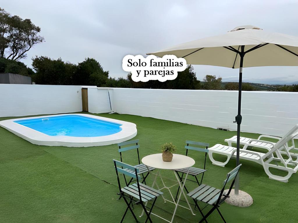 een patio met een parasol en stoelen en een zwembad bij Bungalow para familias y parejas in Conil de la Frontera