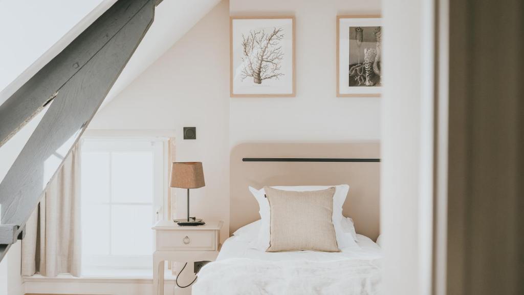 a bedroom with a white bed and two pictures on the wall at Hôtel De La Marine in Arromanches-les-Bains