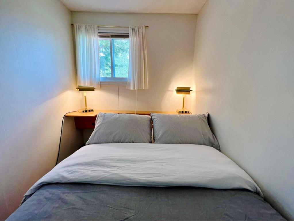 Le Jackrabbit Orford Domaine Cheribourg في Orford: غرفة نوم صغيرة بها سرير مع مصباحين