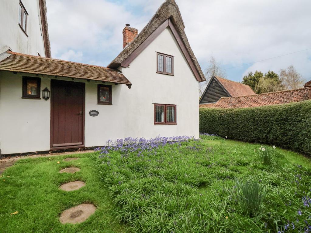 une maison blanche avec une cour verdoyante ornée de fleurs violettes dans l'établissement Bluebell, à Woodbridge