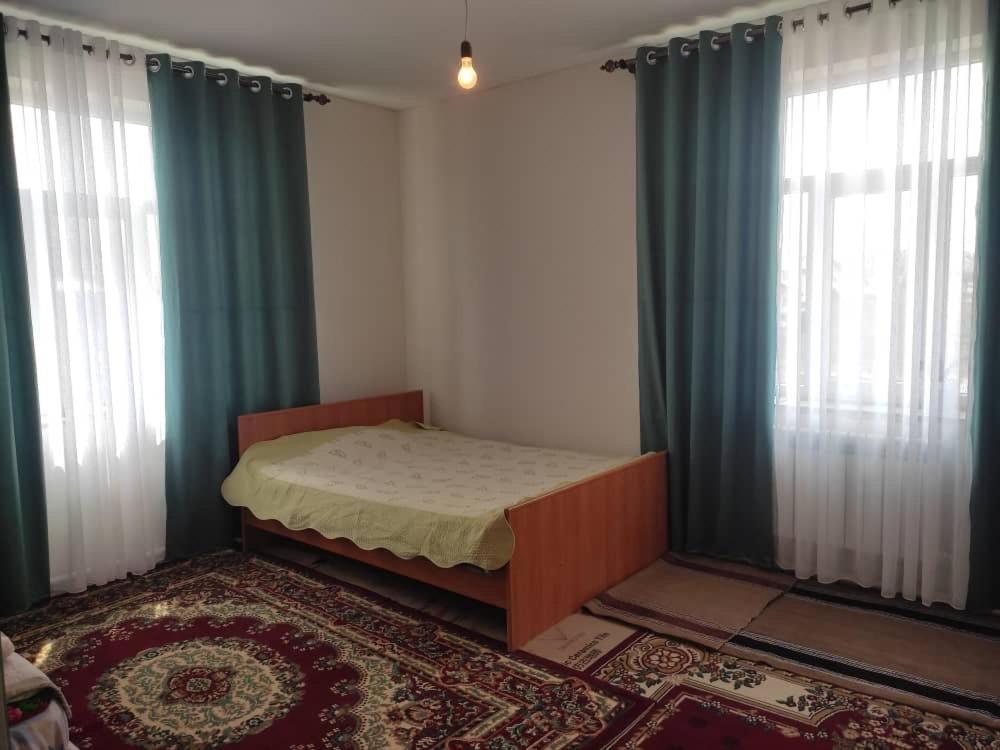 a bedroom with a bed and two windows with curtains at Emir Guest House in Karakol in Karakol