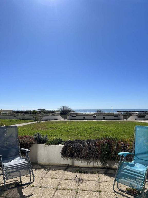 2 chaises assises sur une terrasse en face d'un champ dans l'établissement SUNSET Joli 3 Pièces vue mer piscine Rochelongue Cap d'Agde, au Cap d'Agde