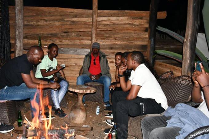 Un groupe de gens assis autour d'un feu dans l'établissement IWACU ECO LODGE, à Rwumba