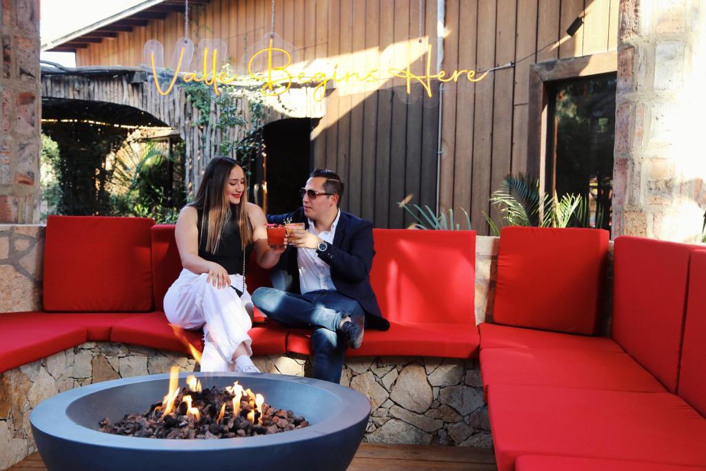 un homme et une femme assis sur un canapé à côté d'un foyer extérieur dans l'établissement Hotel Valle 13 Ruta del Vino, à Valle de Guadalupe