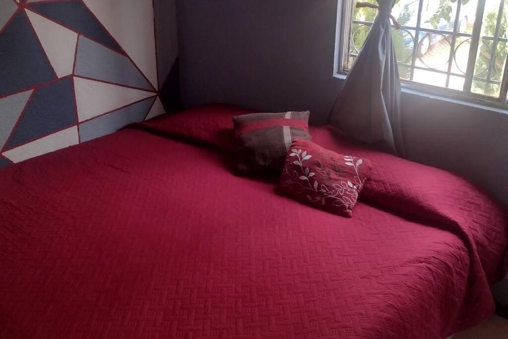 Una cama roja con dos almohadas encima. en casa con vigilancia las 24hrs en Santa Cruz Tecamac