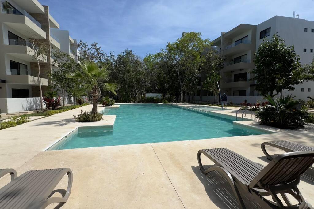 a swimming pool with two chairs and a building at Departamento de Lujo en Playa in Playa del Carmen