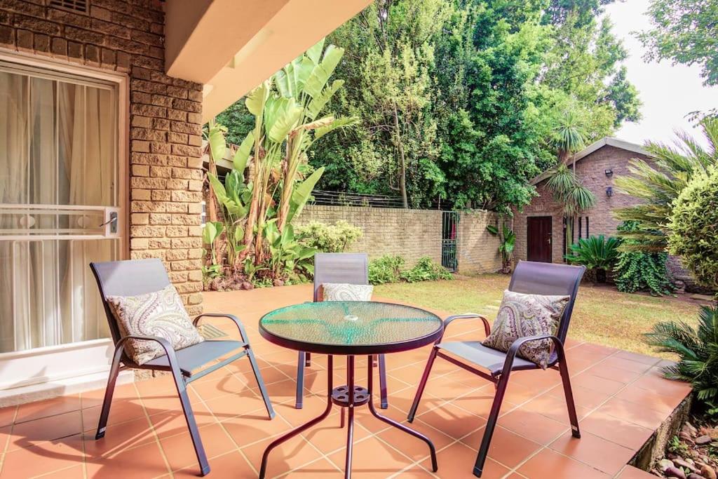 un patio con 3 sillas y una mesa de cristal en The Hide Out - Home away from home en Johannesburgo