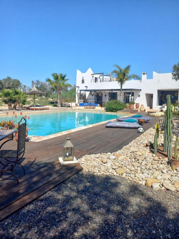 a swimming pool with a wooden deck next to a house at Les jardins de Silona in Essaouira