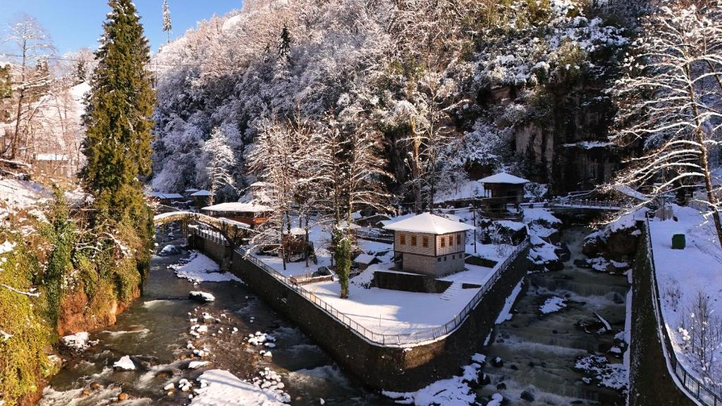 een klein huis in de sneeuw naast een rivier bij Çukur Vadi Evleri in Ardeşen