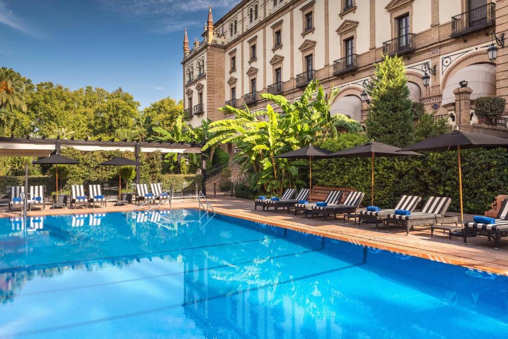 a swimming pool with chairs and umbrellas next to a building at Hotel Alfonso XIII, a Luxury Collection Hotel, Seville in Seville