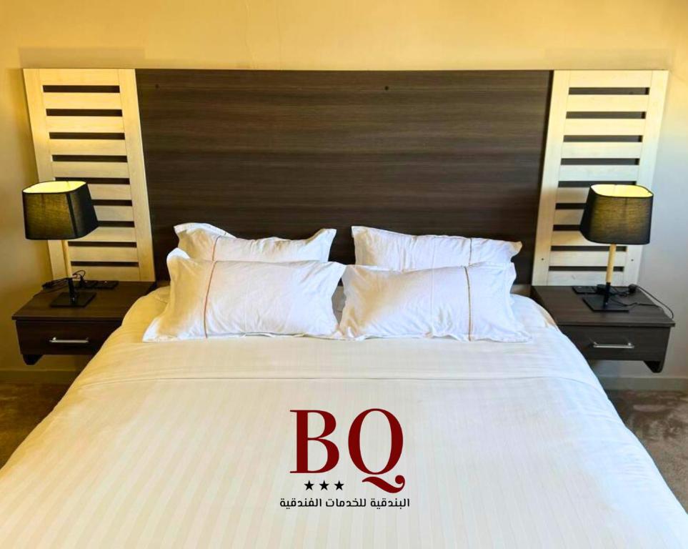 una cama grande con almohadas blancas y un cartel en ella en البندقية للخدمات الفندقية BQ HOTEL SUITES, en Buraidah