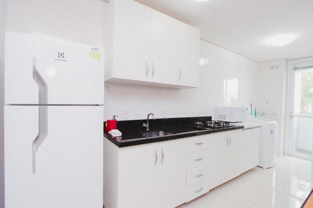 cocina blanca con fregadero y nevera en Apartamento Aconchegante Maia 404, en Caxias do Sul