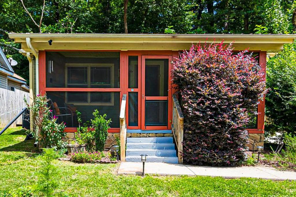 una pequeña casa con una puerta roja y un arbusto en The Sauna Cottage, en Lake Lure