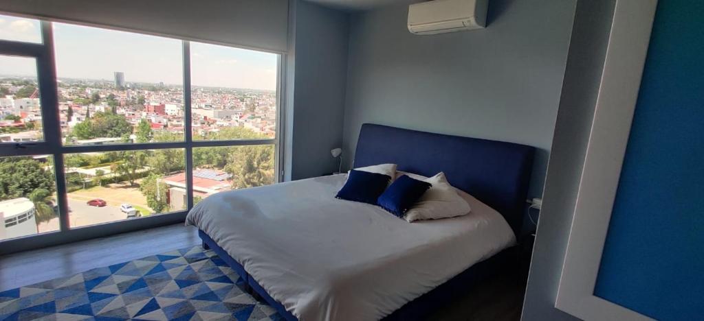 een blauwe slaapkamer met een bed en een groot raam bij Departamento en Puebla (en torre Artema- zona Angelópolis) in Puebla