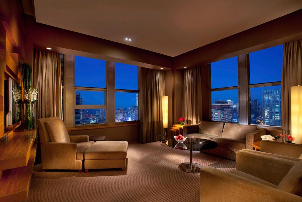 uma sala de estar com um sofá, cadeiras e janelas em Kempinski Hotel Dalian em Dalian