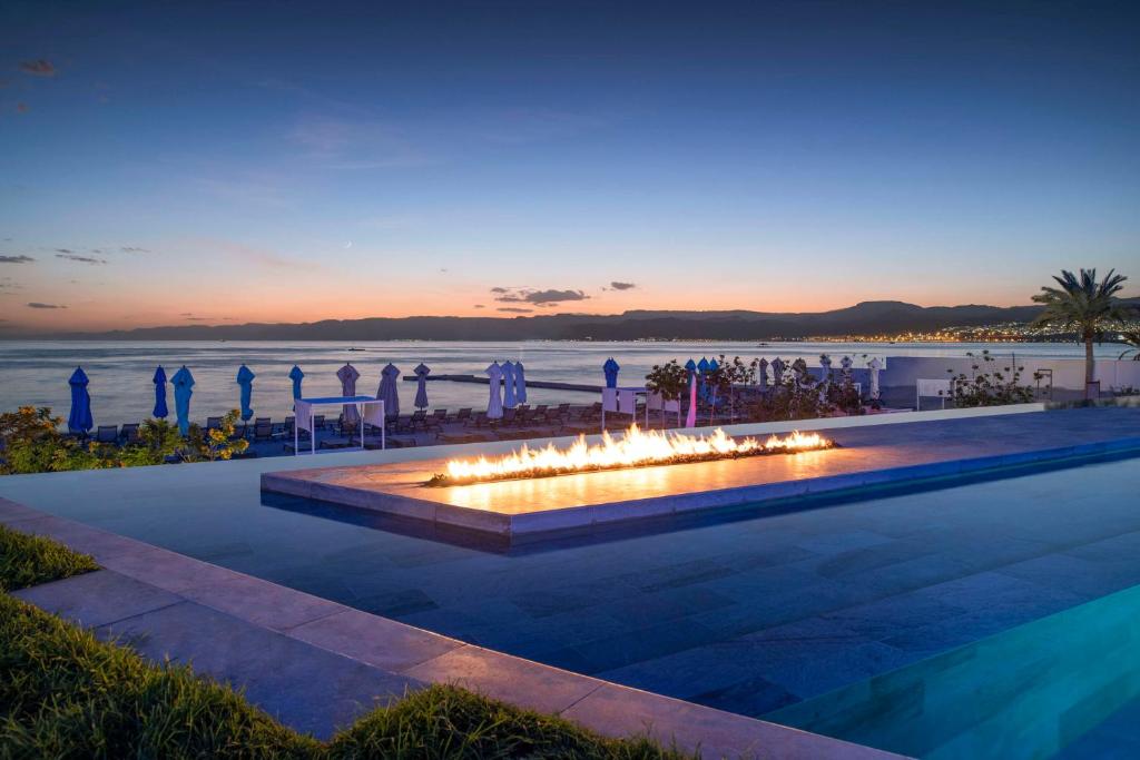 einen Pool mit einer Feuerstelle mit dem Meer im Hintergrund in der Unterkunft Kempinski Hotel Aqaba in Aqaba