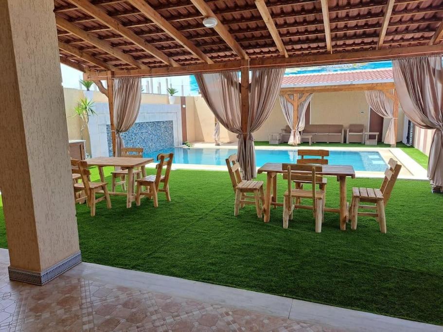 um pátio com mesas e cadeiras ao lado de uma piscina em Villa piscine 4 chambres em Hanshīr Qaşr Ghallāb