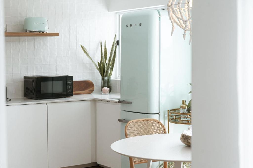 a white kitchen with a refrigerator and a table at The Villa's Mooloolaba in Mooloolaba