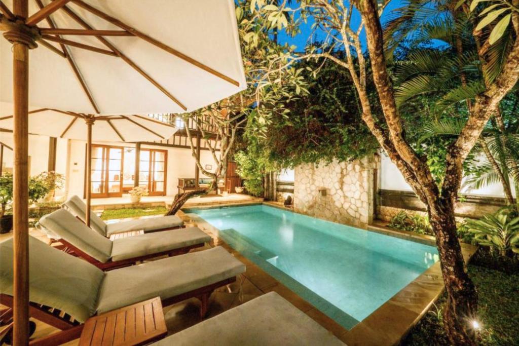 a swimming pool with chairs and an umbrella at Majestic 3 BR Private Pool Villa NE18 in Jimbaran