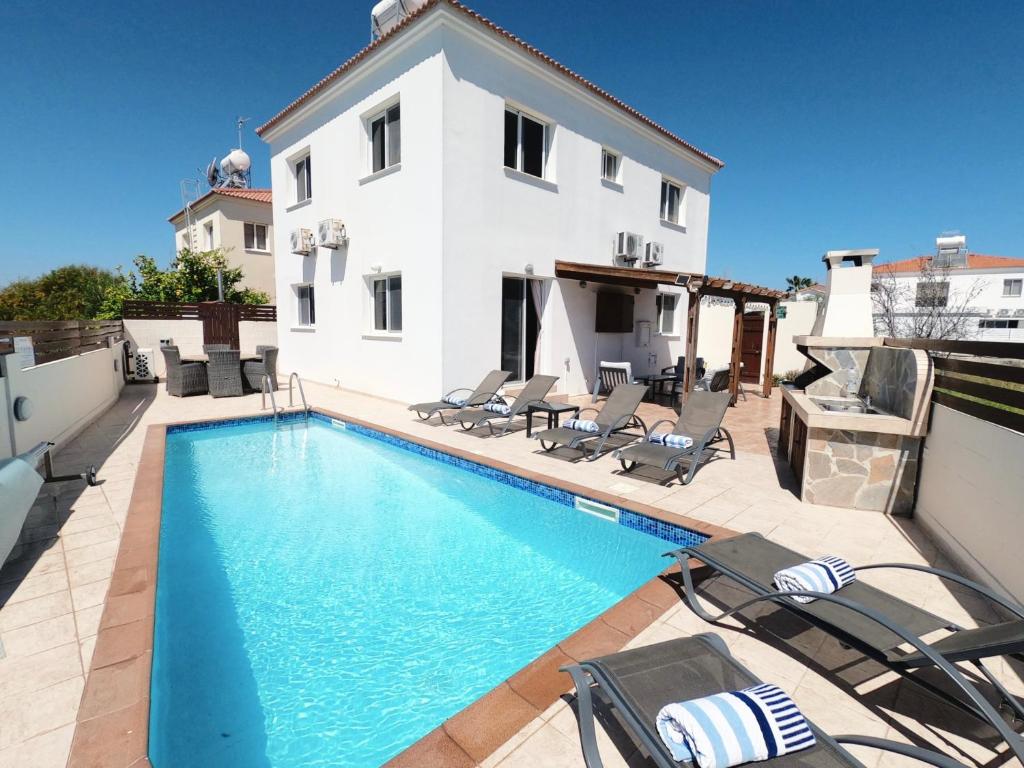 a swimming pool with chairs and a house at Villa Lankas with Heated pool in Ayia Napa