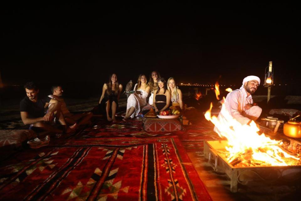 a group of people sitting around a fire on the beach at Adventure Overnight Stay For Groups, Families, Couples, Foods Parties and Events Night in Dubai