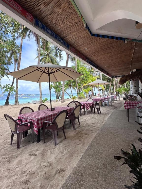 um grupo de mesas e cadeiras com um guarda-sol na praia em Sundown Resort & Austrian Pension House em Boracay