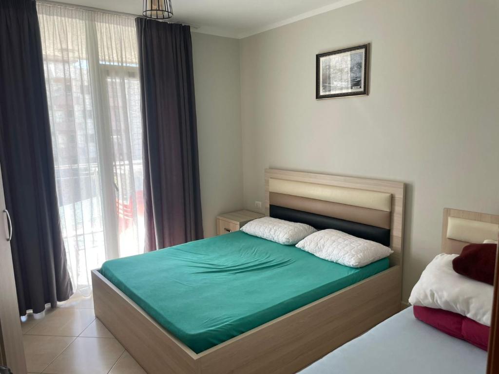 a bedroom with a bed with green sheets and a window at Arber Apartments Deda in Shëngjin