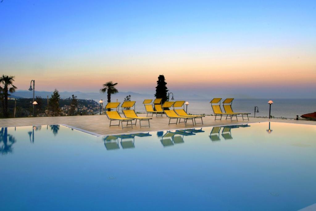 una piscina con sillas amarillas y el océano al atardecer en Residence Villa Beuca, en Cogoleto