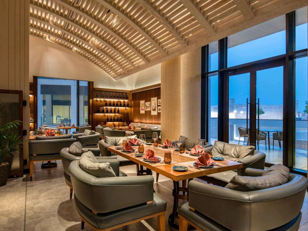 a dining room with tables and chairs and windows at Alwadi Hotel Doha - MGallery Collection in Doha