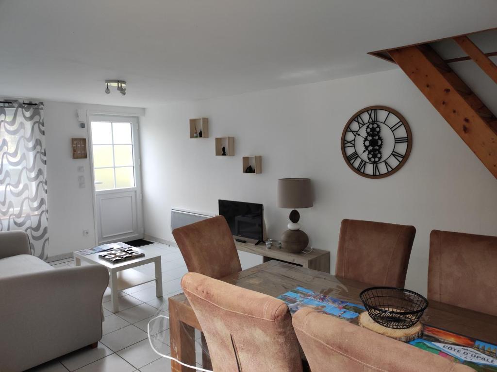 a living room with a table and a clock on the wall at La petite trapue in Desvres