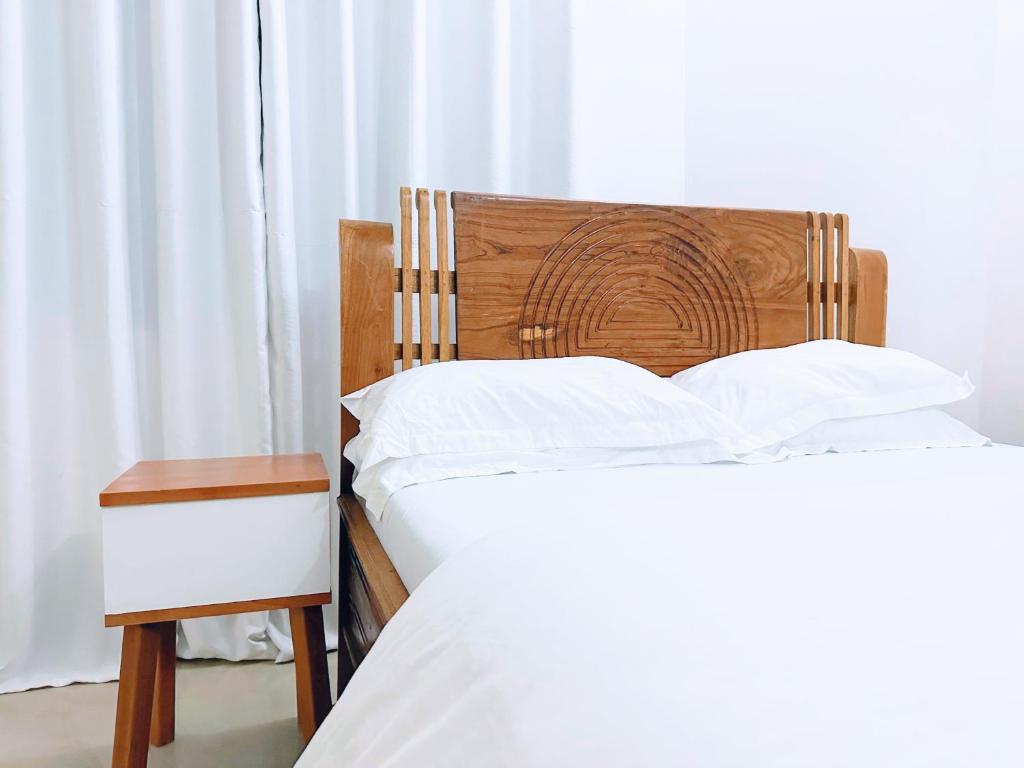 two beds with white sheets and a wooden headboard and a table at Wakanda Elegant Apartment with Wi-Fi by Monalisa in Morogoro