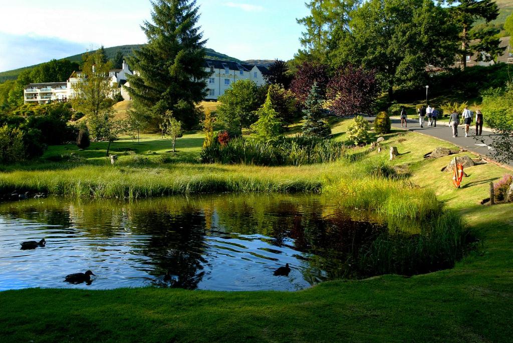 a pond in a park with people walking around it at Macdonald Forest Hills Resort in Aberfoyle