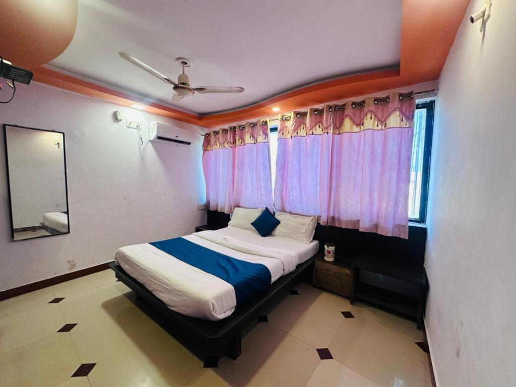 a bedroom with a bed with blue sheets and pink curtains at HOTEL SHREE DWARKA in Dwarka