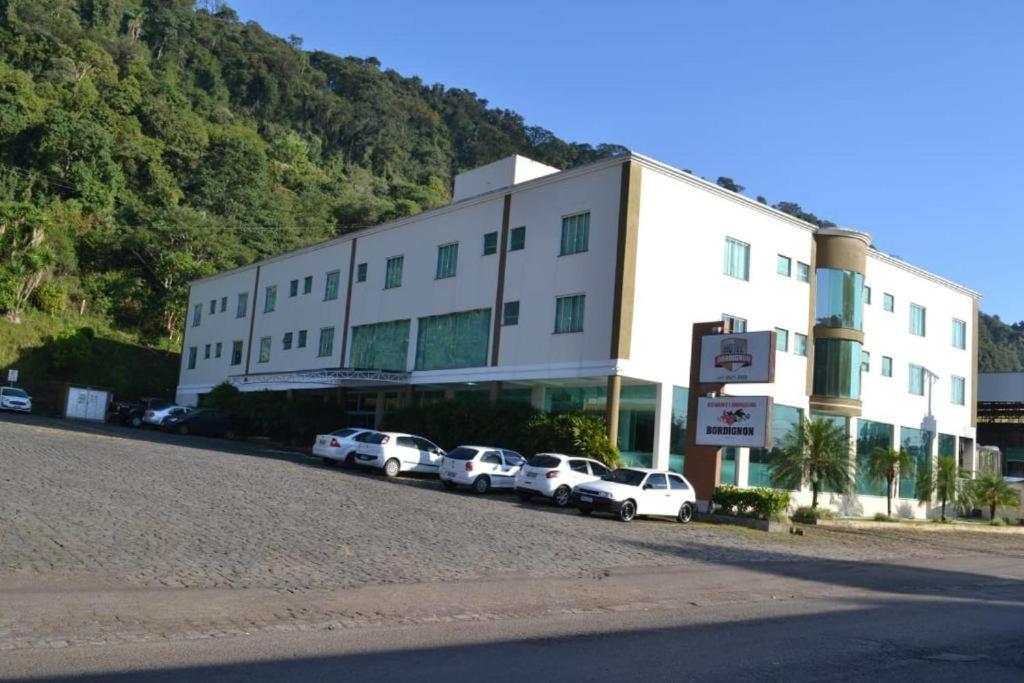 un gran edificio blanco con coches estacionados frente a él en Hotel e Restaurante Bordignon, en Joaçaba