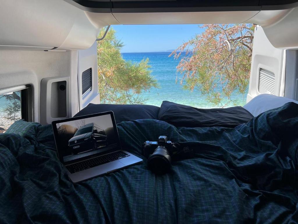 kamera i laptop na łóżku z widokiem na ocean w obiekcie Reunion in Greece Campervan w mieście Drafí