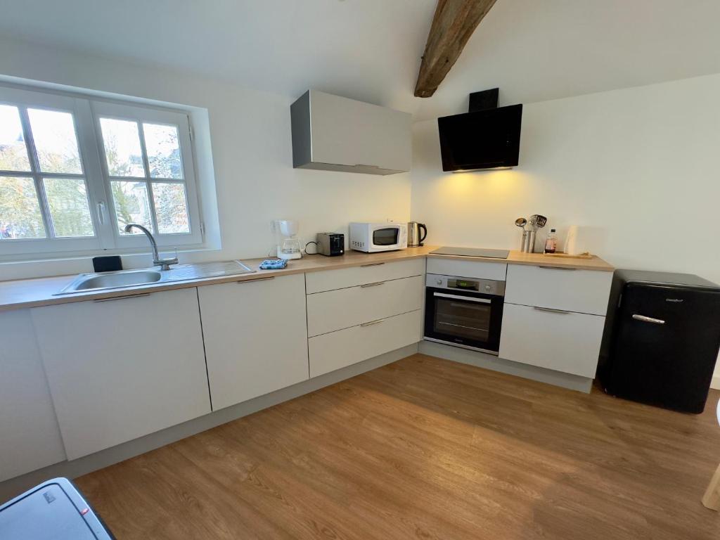a kitchen with white cabinets and a black refrigerator at Appartement Le Voltaire centre ville climatisé in Saumur